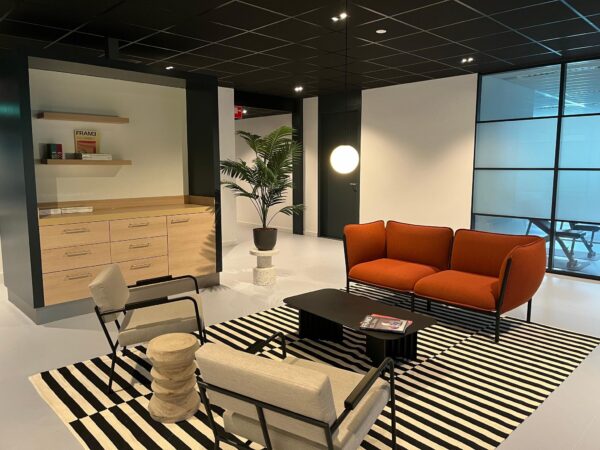 Moderne wachtruimte met een oranje bank, designstoelen, zwart-wit gestreept vloerkleed en stijlvolle inrichting bij De Wel.